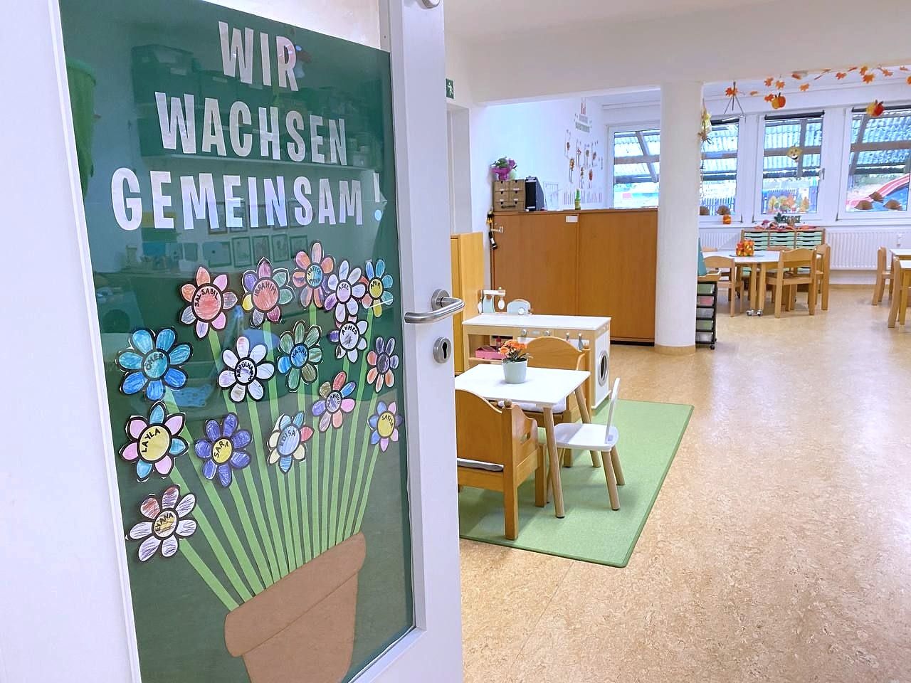 Tür mit dem Plakat "Wir wachsen gemeinsam" und Blick in den Gruppenraum